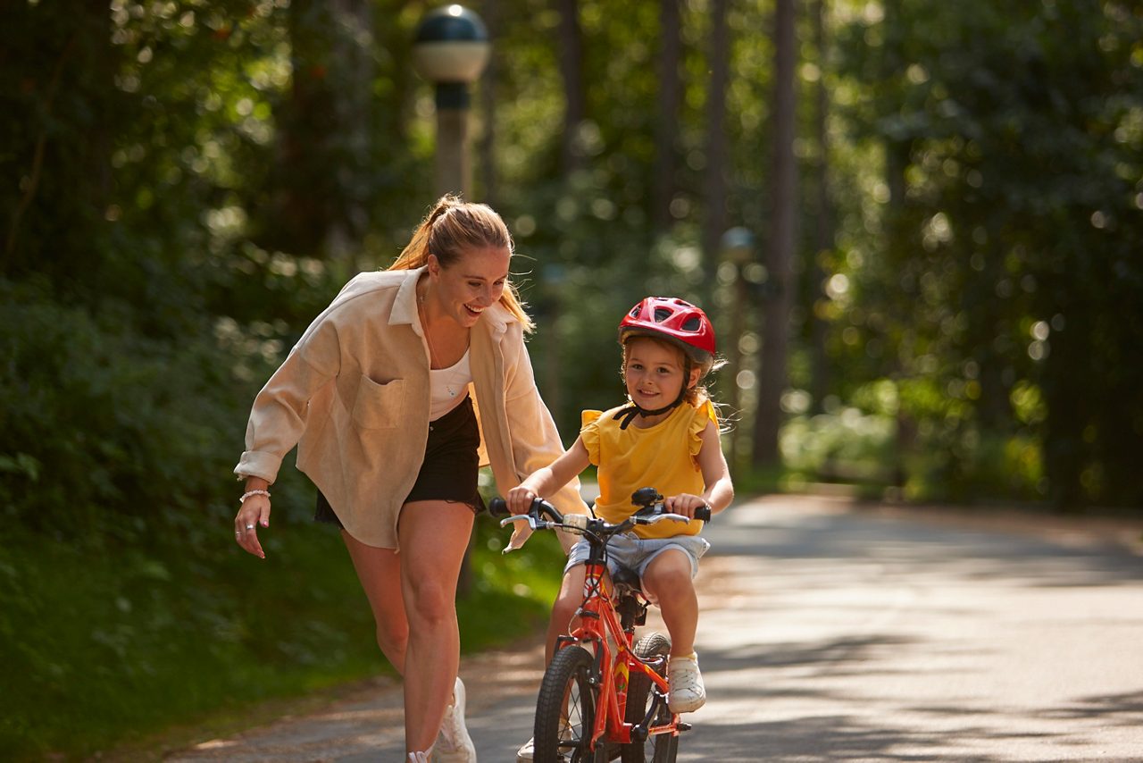 A mother helping her child cycle through the forest.